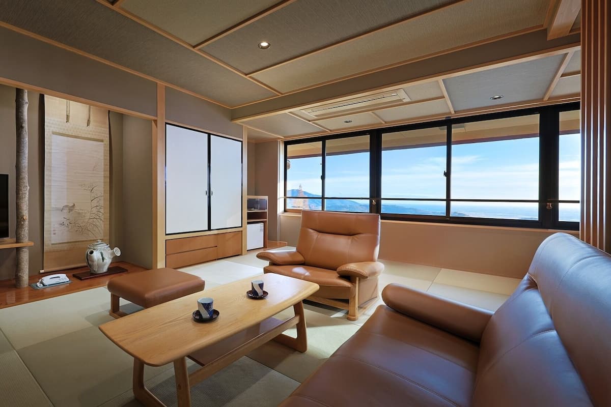 A modern living room with a sofa, a coffee table, and a television. There is a large window with a view of the mountains.