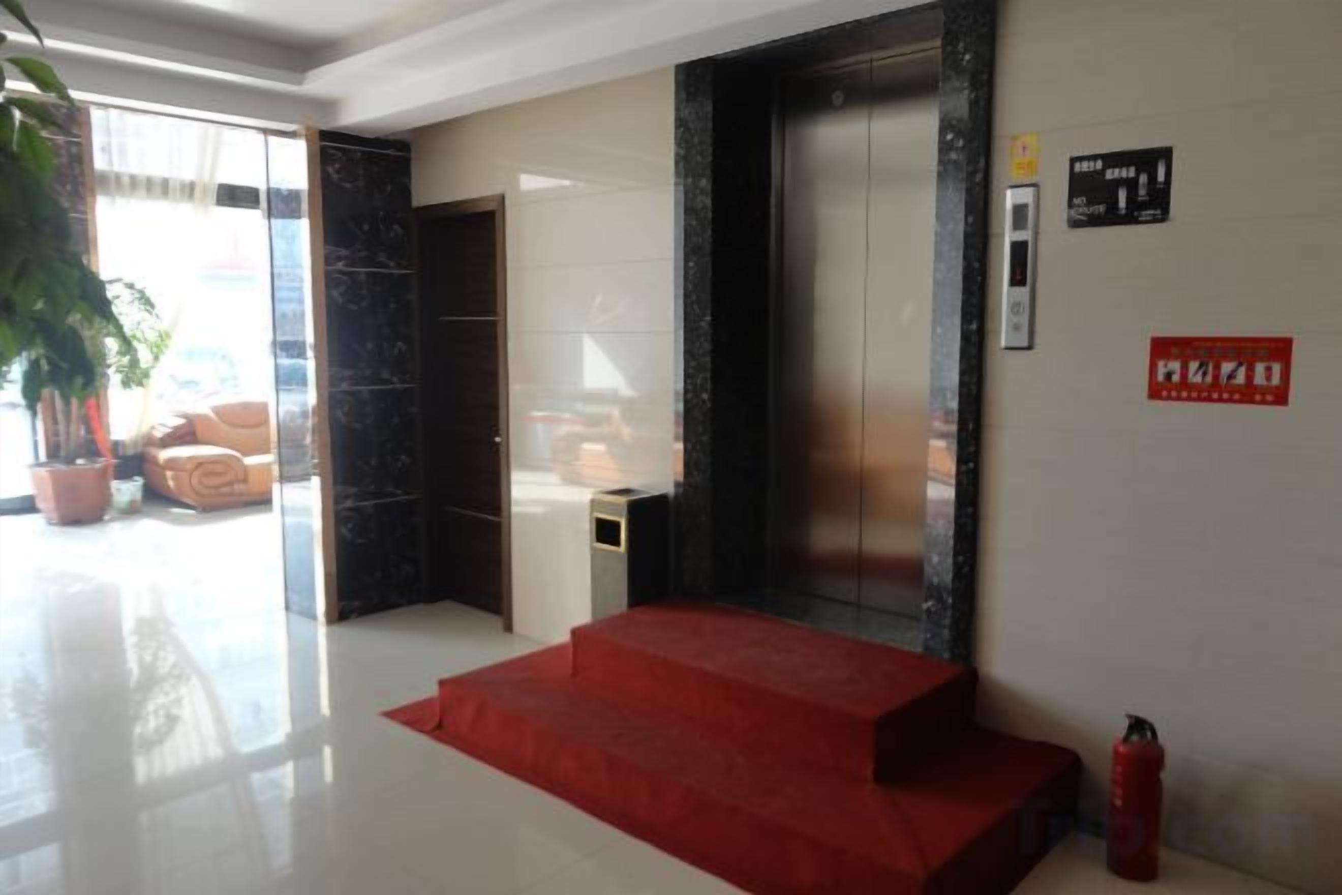 Vestíbulo de hotel con alfombra roja, una escalera, un mostrador de recepción, una planta en maceta y un extintor.