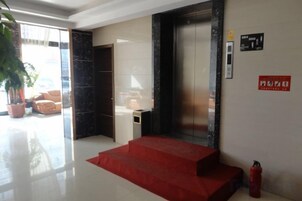 Vestíbulo de hotel con alfombra roja, una escalera, un mostrador de recepción, una planta en maceta y un extintor.