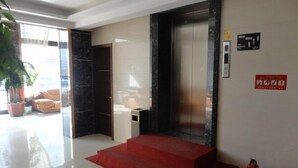 A hotel lobby with a red carpet leading to an elevator, a fire extinguisher on the wall, and a plant in the corner. - Senli Hotel (Sanmen)