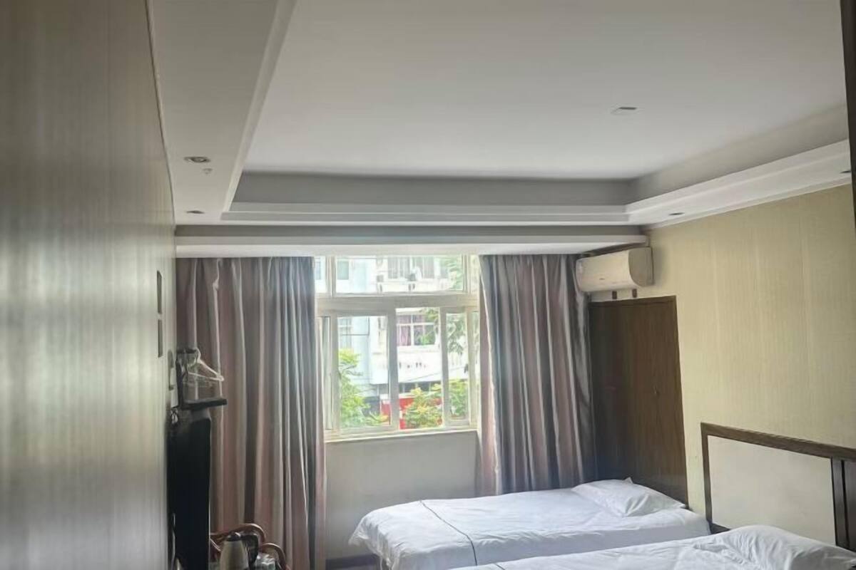 A hotel room with a bed, a window with curtains, a wardrobe, and a door.