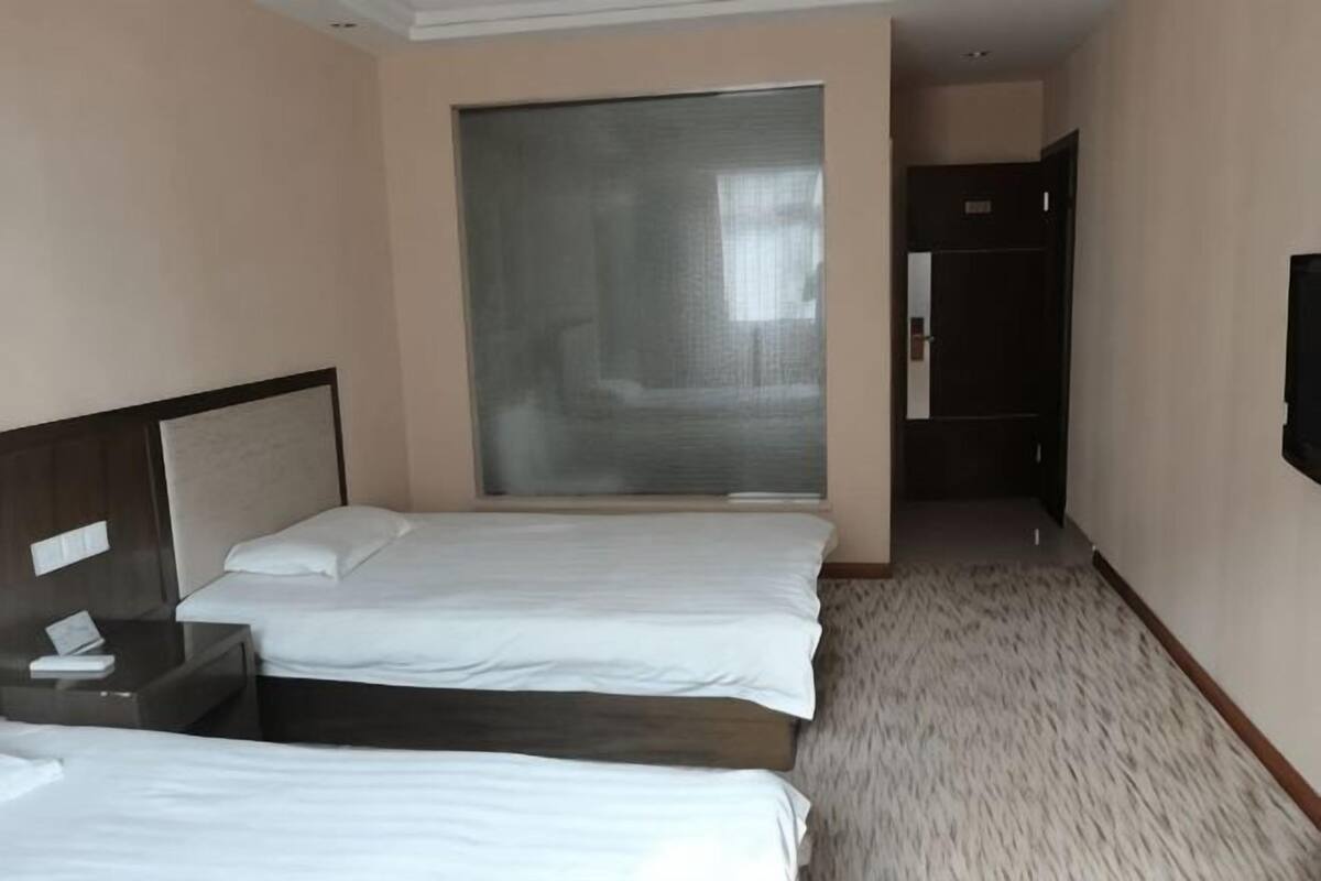 A hotel room with two beds, a large window, a door, and a flat-screen TV.