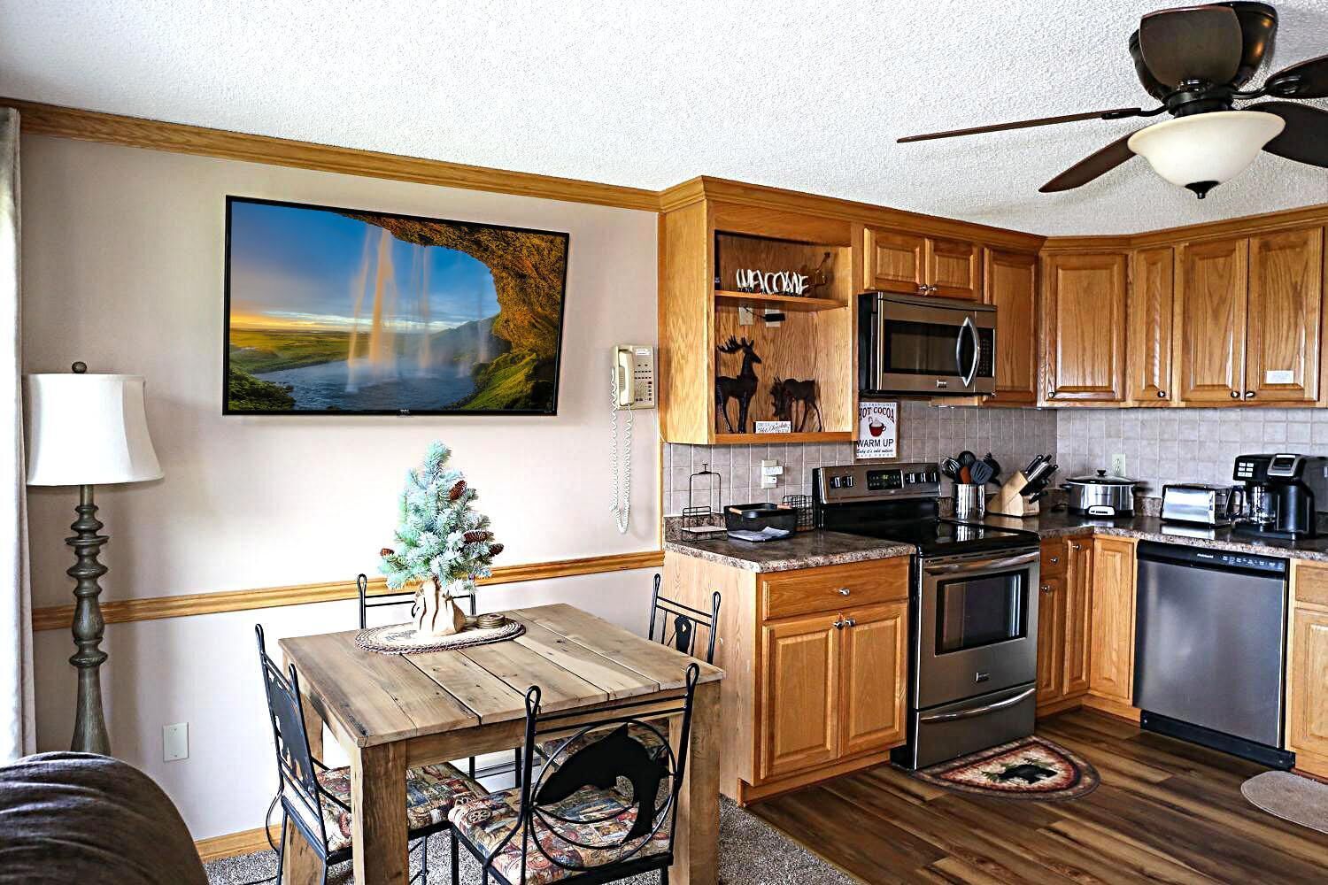 A modern kitchen with wooden cabinets, a dining table with chairs, a ceiling fan, and a large painting on the wall.