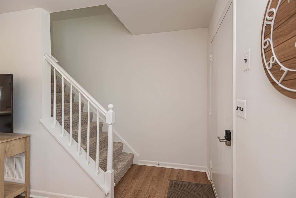 Una escalera con barandillas blancas, piso de madera y un reloj fijado a la pared.