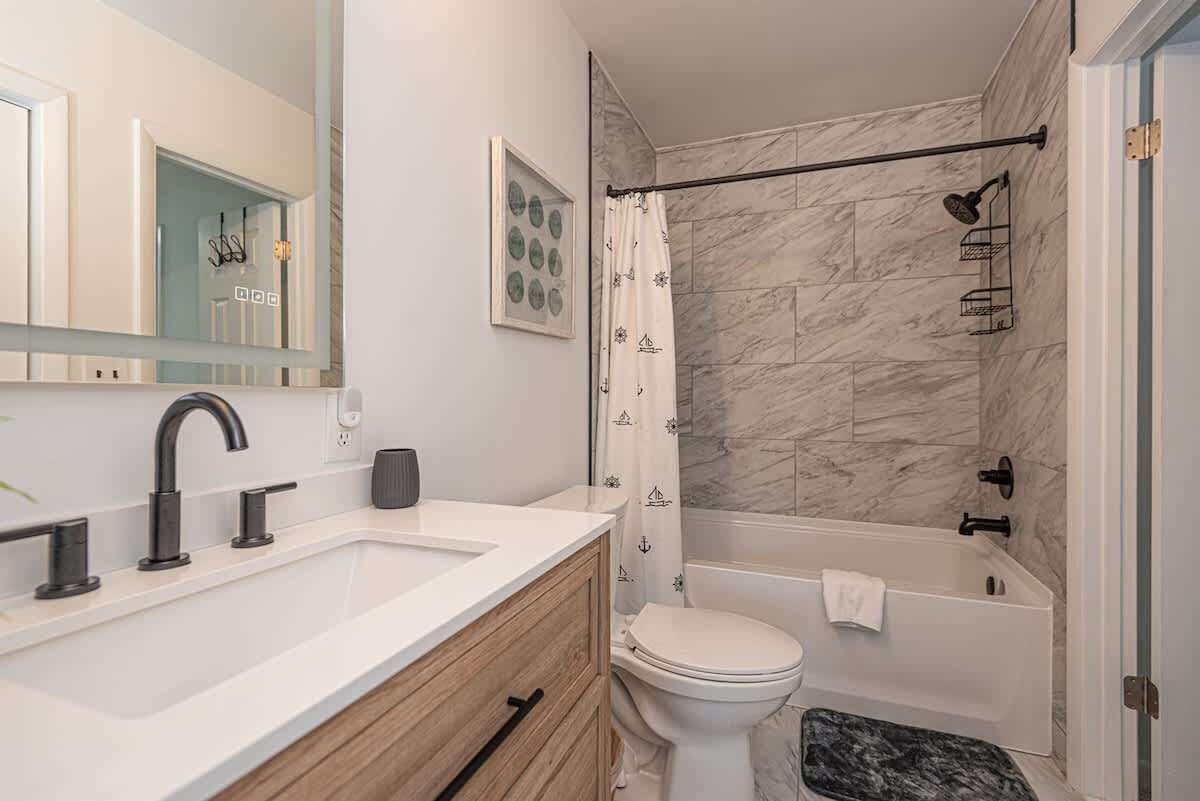 A bathroom with a white sink, a toilet, a bathtub, and a shower curtain with a nautical pattern.