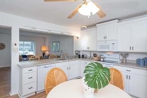 A modern kitchen with white cabinetry, a dining area with wicker chairs, and a ceiling fan. - Waterfront Getaway with Boat Slip (Ocean City)