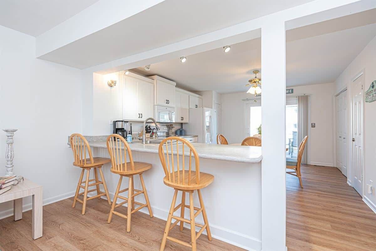 A modern kitchen with white cabinets, a central island with bar stools, and a visible microwave.