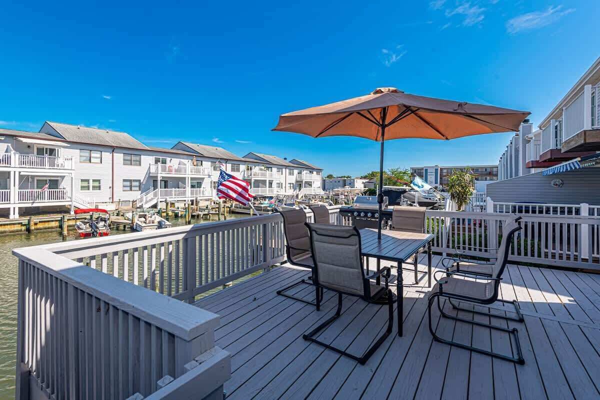 A deck with outdoor furniture, a flag, and a view of a marina with boats.