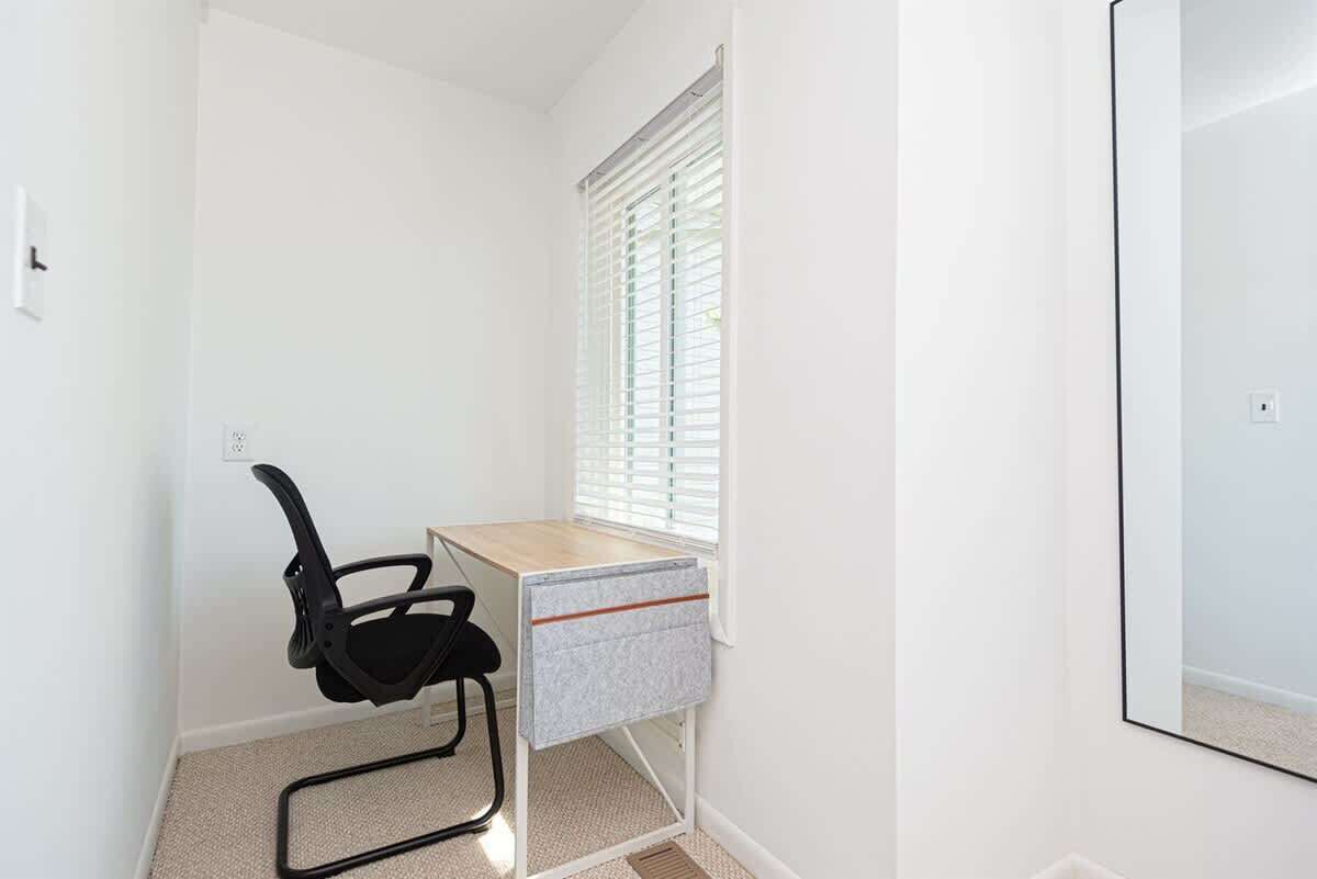 A small, well-lit room with a desk, chair, and window with blinds.