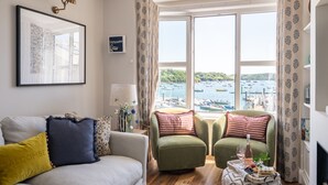 A cozy living room with a sofa, two armchairs, a coffee table, and a view of boats on a lake through large windows.