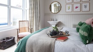 A bedroom with a bed, a dresser, a chair, a window, and a wall with framed botanical prints.
