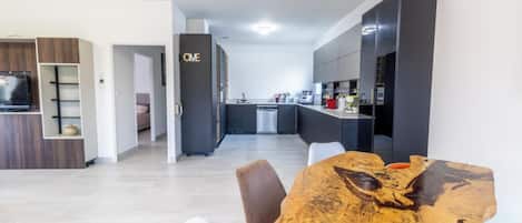 A modern kitchen with dark cabinetry, a dining area with a wooden table, and a visible 'ONE' sign on the wall.