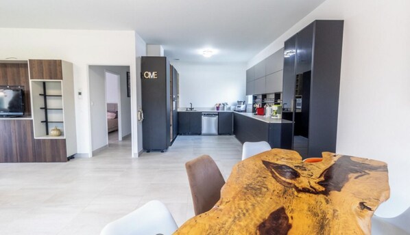 Eine moderne Küche mit dunklen Schränken, ein Essbereich mit einem Holztisch und ein gut sichtbares Schild mit der Aufschrift 'ONE' an der Wand.