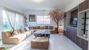 Ein modernes Wohnzimmer mit einem Ecksofa, einem Glastisch und einem Fernseher auf einem Holzregal.