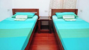 A room with two single beds, each with a wooden headboard and a green bedspread. There is a small wooden nightstand between the beds, and a red tiled floor. - C Star Travellers Inn (Oslob)