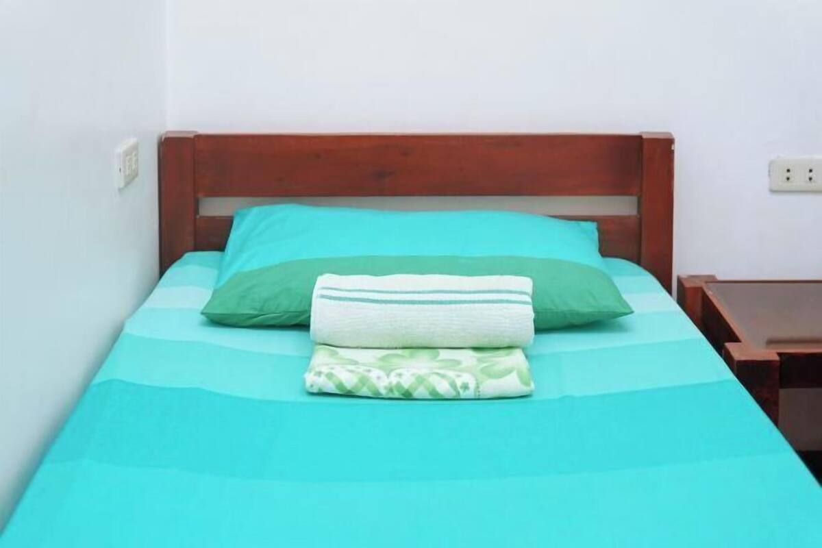 A single bed with a wooden headboard, a teal bedspread, and two pillows.