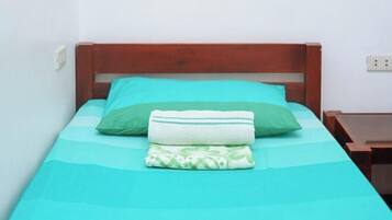 A single bed with a wooden headboard, a teal bedspread, and two pillows.
