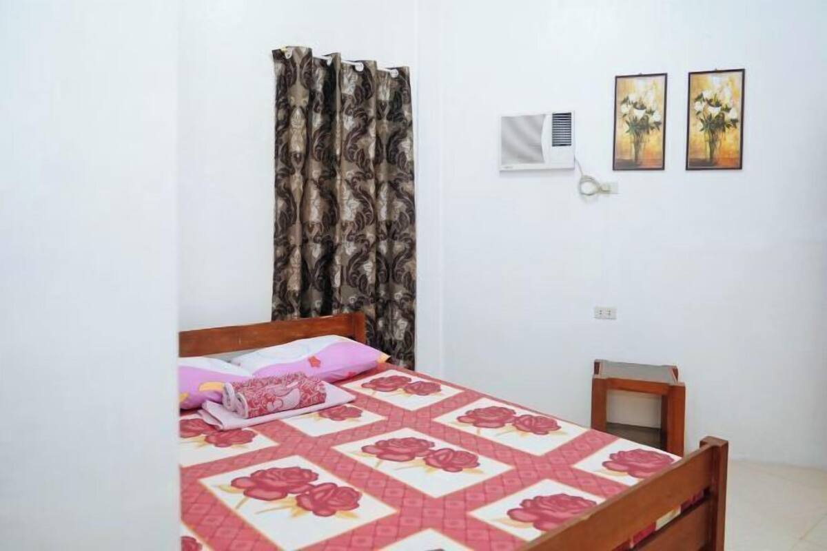 A bedroom with a bed, a nightstand, a wall-mounted air conditioner, and two framed pictures.