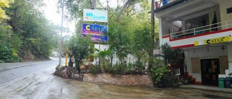 A hotel named '489 Roussin' with a 'C-Star' sign, a balcony, and a wet road.
