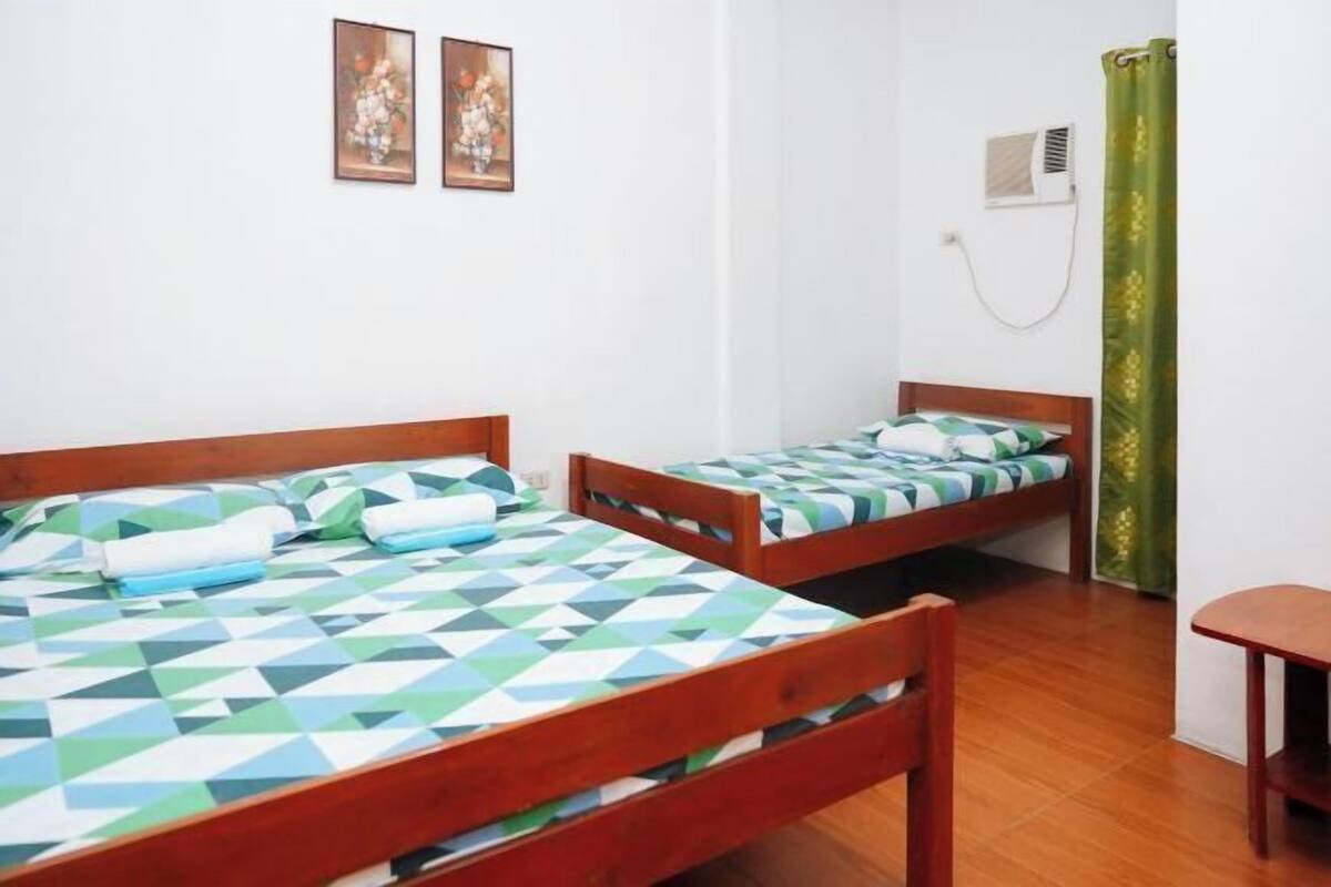 A room with two wooden beds, a small table, and a wall-mounted air conditioner.