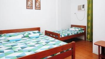 A room with two wooden beds, a small table, and a wall-mounted air conditioner.