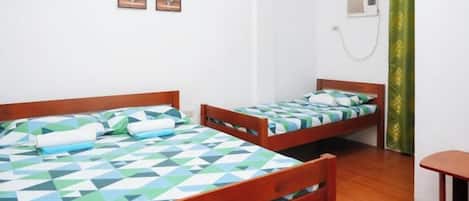 A room with two wooden beds, a small table, and a wall-mounted air conditioner.