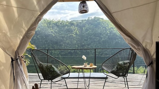 A tent with a view of a forested landscape. Inside, there are two chairs and a table with a flower and a cup. - encanto Toscano (Quimbaya)