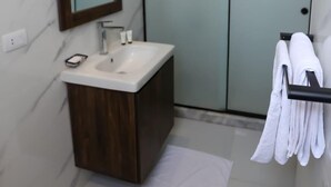 Une salle de bain moderne avec un mur en marbre, un meuble-lavabo en bois, un lavabo blanc, un miroir et une cabine de douche en verre.