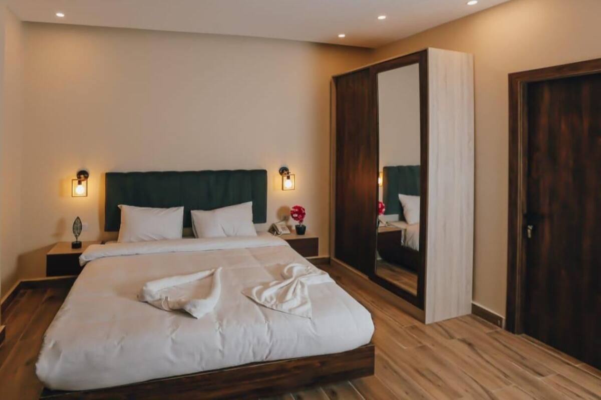 Ein ordentlich bezogenes Bett mit weißen Leinen, ein dunkles Holz-Kopfteil und zwei Nachttischlampen.