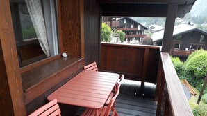 Ein Holzbalkon mit Tisch und Stühlen, mit Blick auf eine gebirgige Gegend mit Häusern.