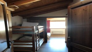 Ein Zimmer mit einem Etagenbett, einem Holzschrank und einer Tür zu einem anderen Raum.
