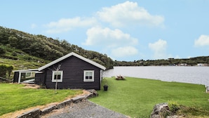 Una cabaña negra con un patio cubierto de césped y vista al lago.