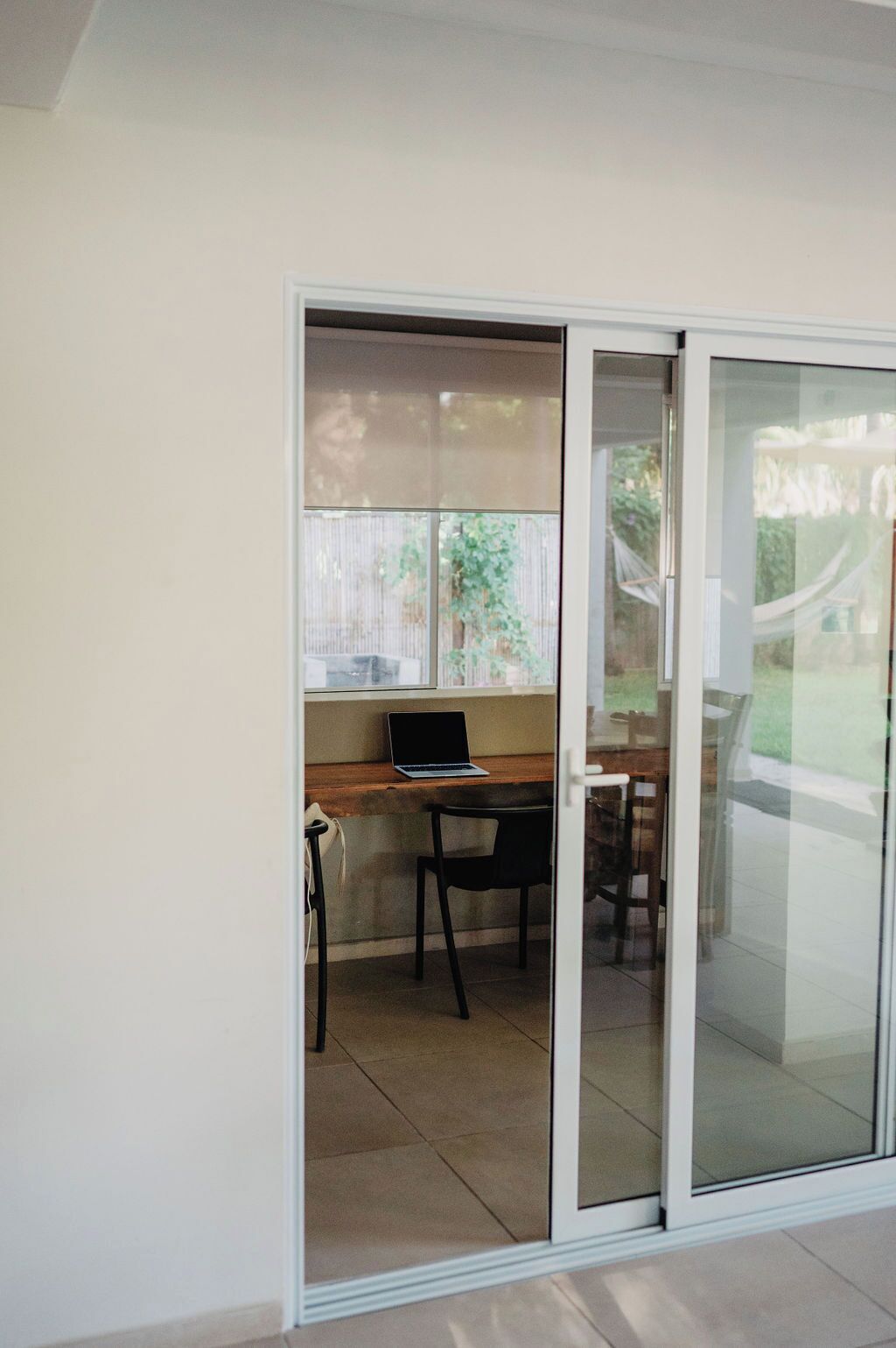 Une pièce dotée d’une porte-fenêtre coulissante donnant sur un balcon, d’un ordinateur portable posé sur un bureau en bois et d’une chaise.