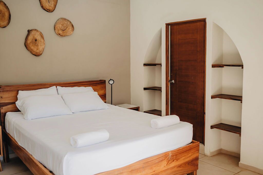 A neatly made bed with white linens and a wooden headboard, a wooden wardrobe, and a wall with wooden wall art.