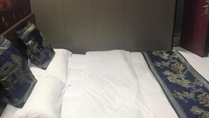 A bed with white bedding and a blue floral-patterned bedspread.
