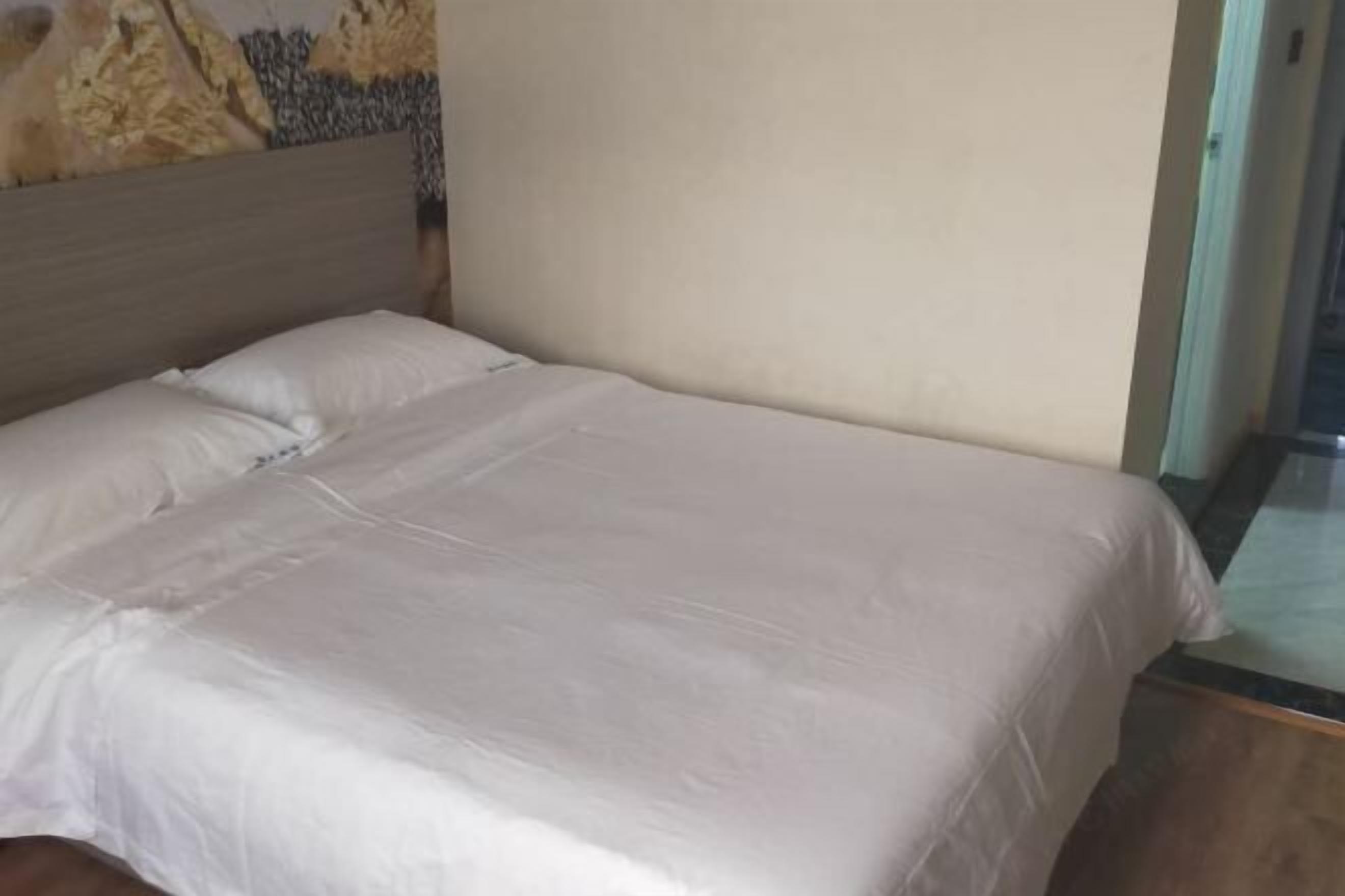 A single bed with a wooden headboard, a plain wall, and a glass door.