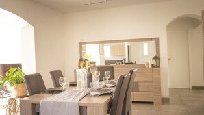 A modern dining area with a wooden table set for four, a kitchen in the background, and a large mirror above the counter. - Maison Loutina, Villa 5-10 min à Pied du Centre (L'Isle-sur-la-Sorgue)