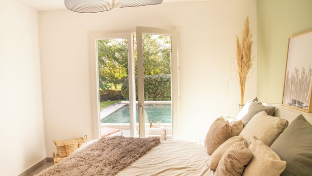 A bedroom with a bed, a large window, and a view of a swimming pool. - Maison Loutina, Villa 5-10 min à Pied du Centre (L'Isle-sur-la-Sorgue)