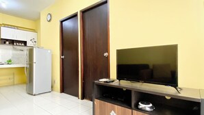 A modern kitchen with a refrigerator, a microwave, and a coffee machine. There is a wooden cabinet with a television on top. - Warm And Cozy 2Br Mutiara Bekasi Apartment (Bekasi)