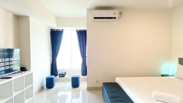 Habitación de hotel con cama, televisión, escritorio con computadora y ventana con cortinas.