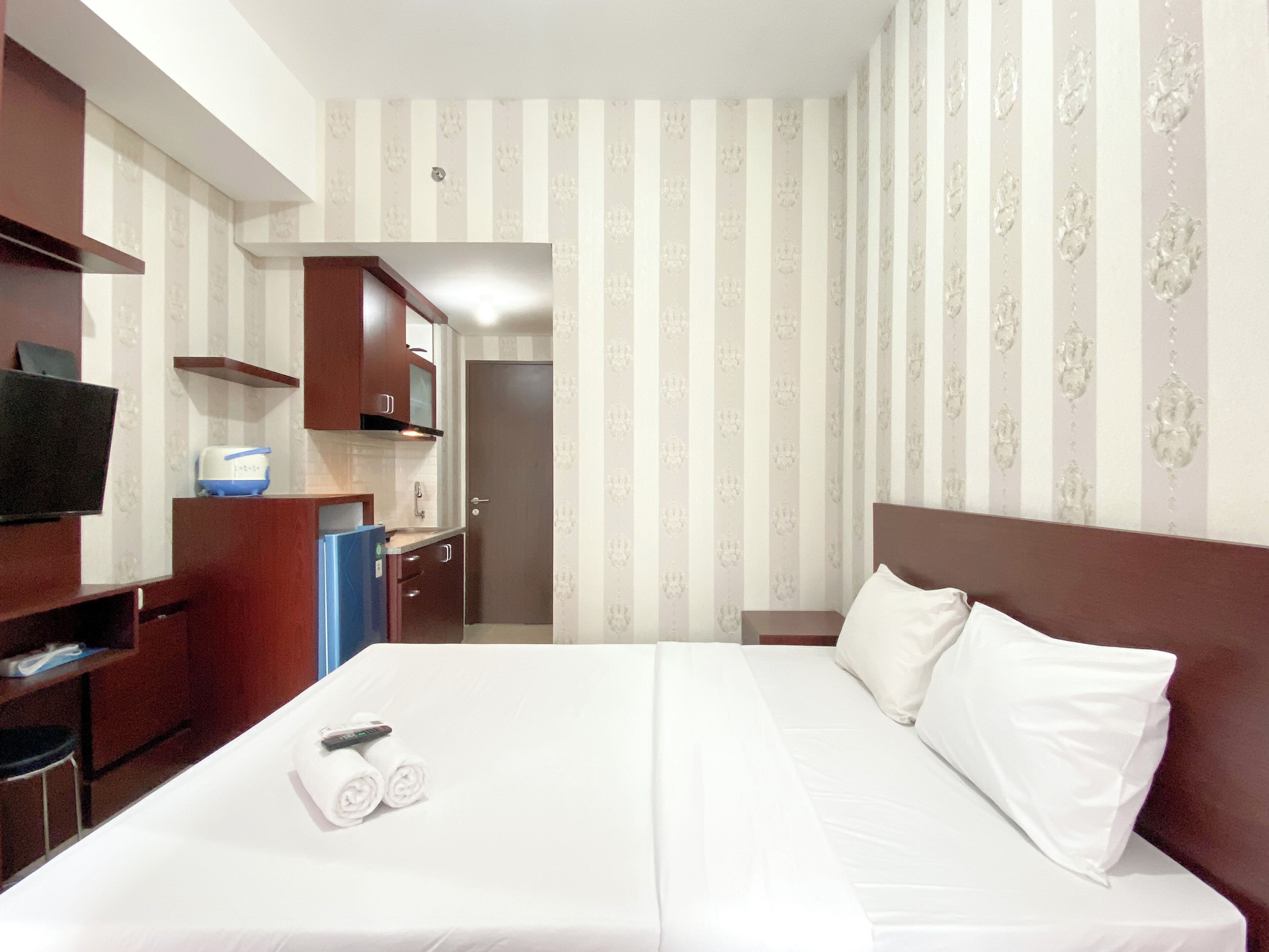 A hotel room with a bed, a TV, a small kitchenette, and a bathroom.