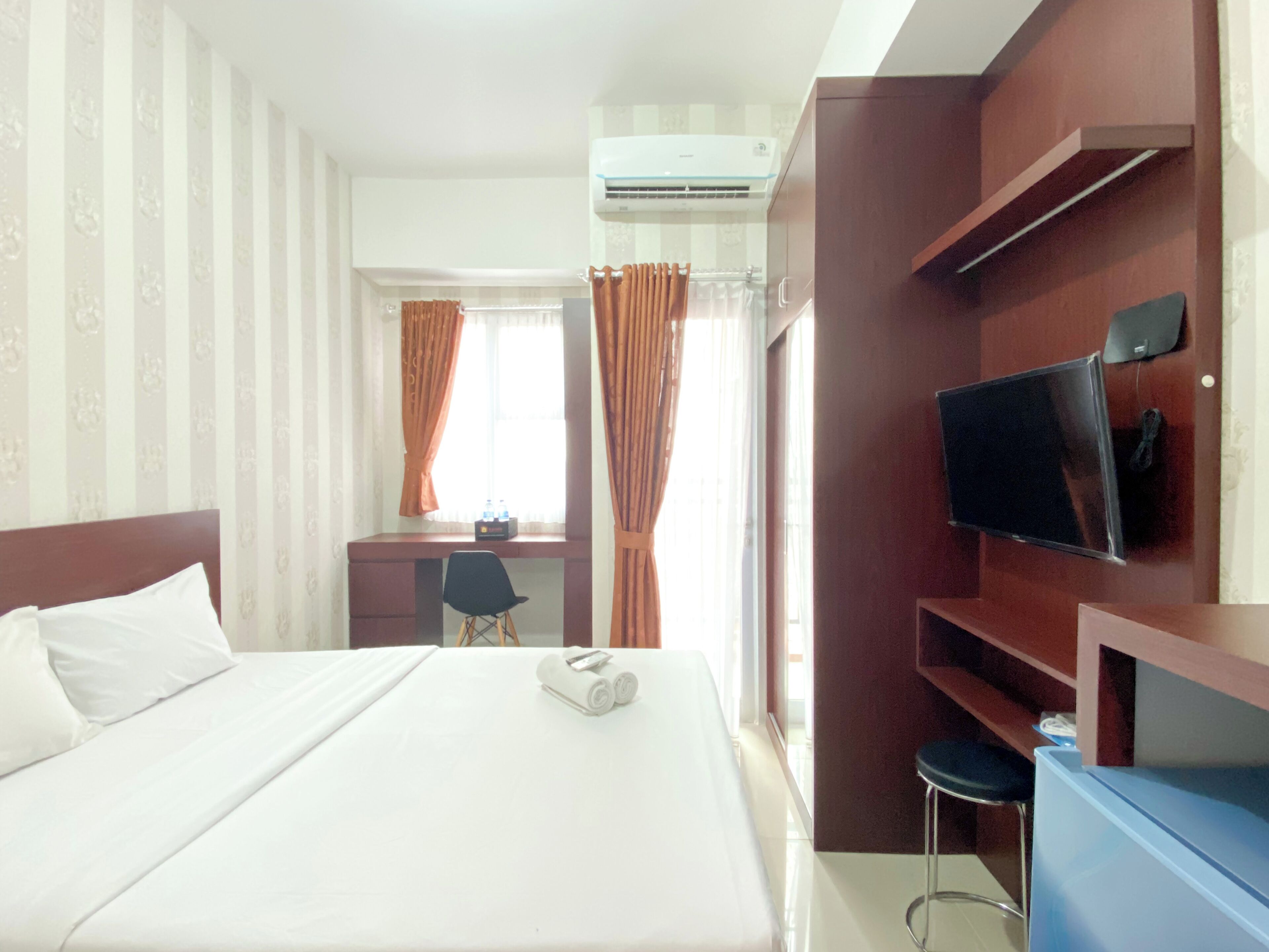 A hotel room with a bed, a desk, a chair, a television, and an air conditioning unit.