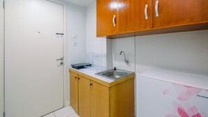 A compact kitchen with wooden cabinets, a white countertop, a stainless steel sink, and a white refrigerator. - Homey And Tidy Studio Dramaga Apartment Near Ipb (Dramaga)