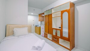 A hotel room with a bed, a wooden wardrobe, and a small kitchenette. - Homey And Tidy Studio Dramaga Apartment Near Ipb (Dramaga)