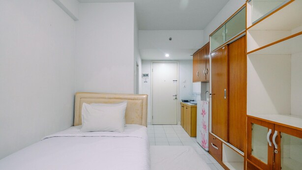 A bedroom with a bed, wooden wardrobe, and a small kitchenette in the background. - Homey And Tidy Studio Dramaga Apartment Near Ipb (Dramaga)