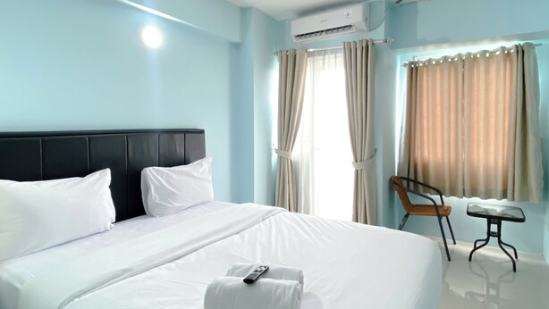 A hotel room with a large bed, a chair, a small table, and an air conditioning unit. - Minimalist Studio Grand Sentraland Karawang Apartment (Karawang)