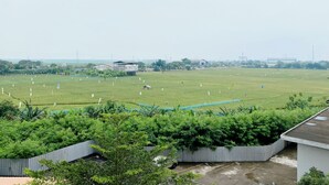 A large open field with several small buildings and a few trees in the foreground. - Minimalist Studio Grand Sentraland Karawang Apartment (Karawang)