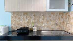 A kitchen with light wood cabinets, a black countertop, a stainless steel sink, and a patterned backsplash. - Minimalist Studio Grand Sentraland Karawang Apartment (Karawang)