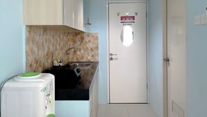 A compact kitchen with a sink, a stove, and cabinets. A 'No Smoking' sign is visible on the door. - Minimalist Studio Grand Sentraland Karawang Apartment (Karawang)