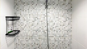Una doccia con soffione circolare e parete rivestita di piastrelle a pois.